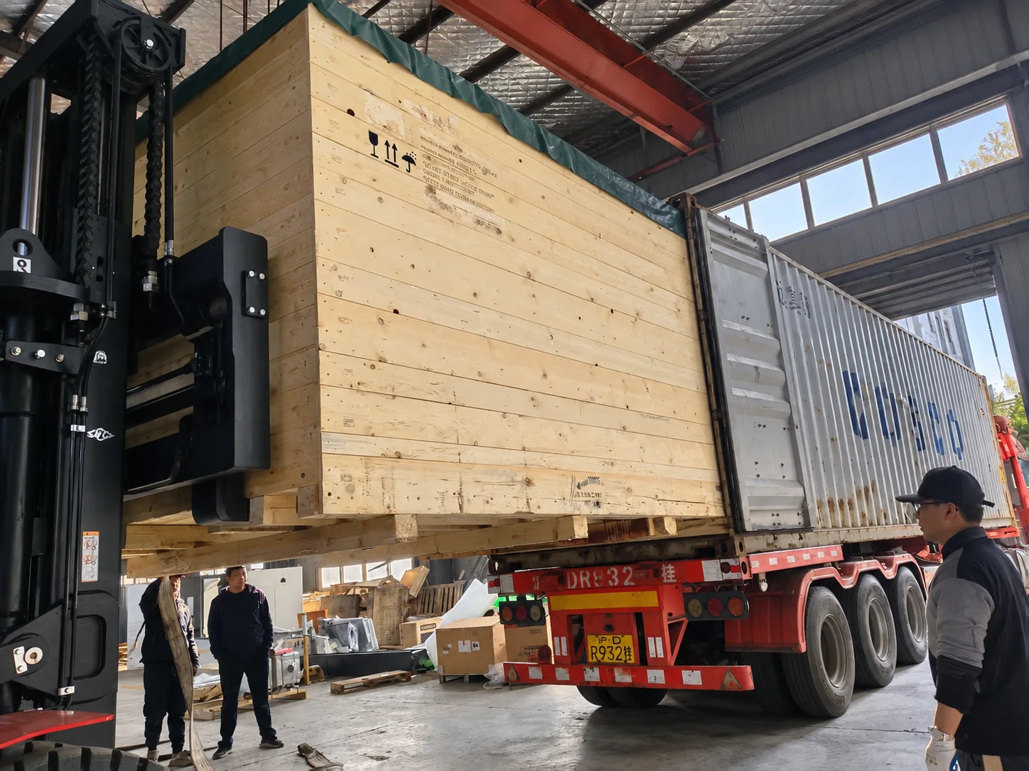 Forklift loading a large wooden machinery crate into a shipping container at a warehouse in China
